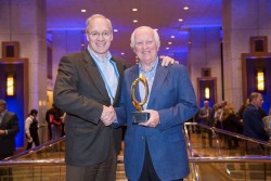 two men shaking hands holding gold trophy dispenser amenities