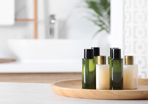 Wooden tray with mini bottles of cosmetic products on white table in bathroom. Space for text